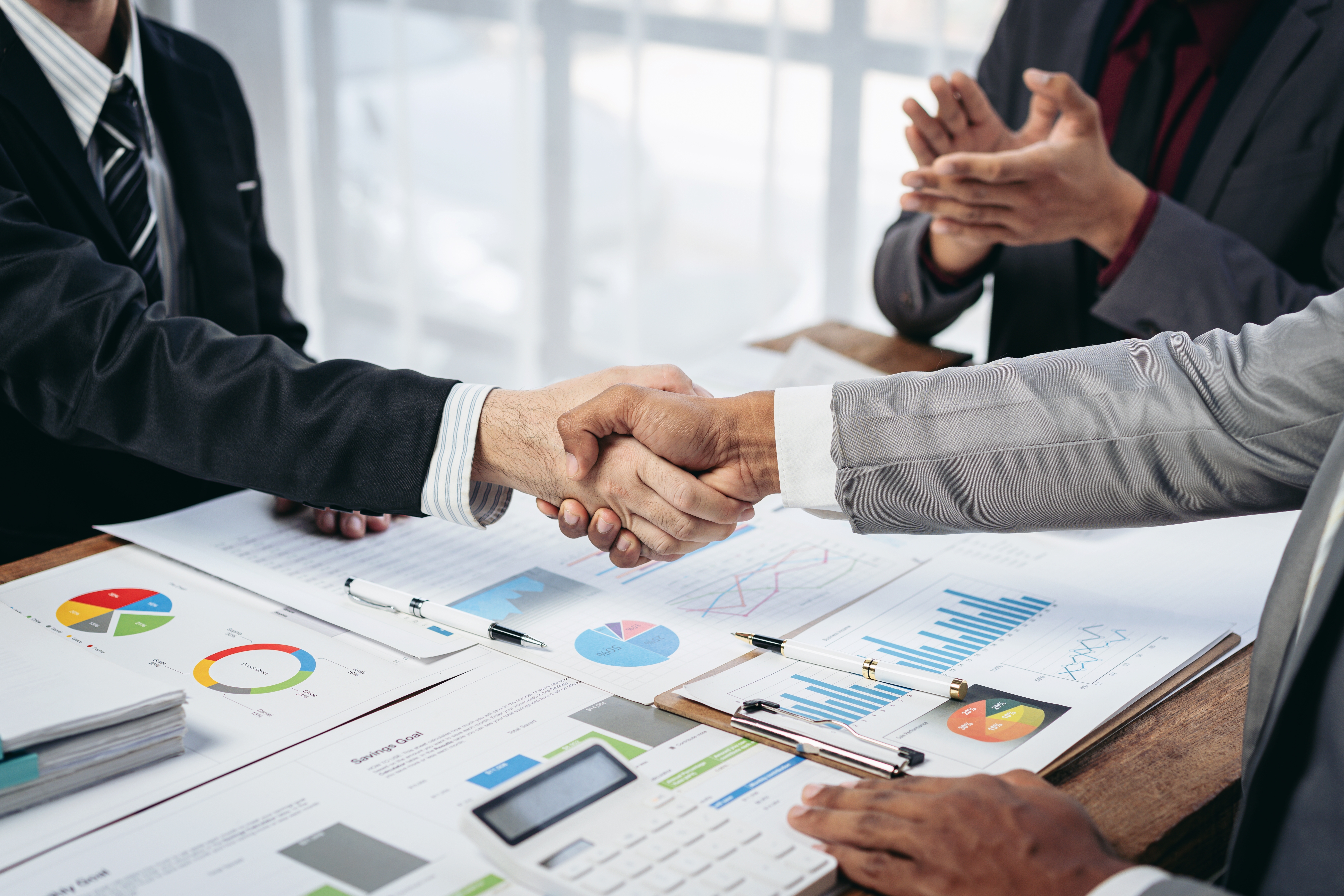 Business men shaking hands with numbers on papers under their hands.